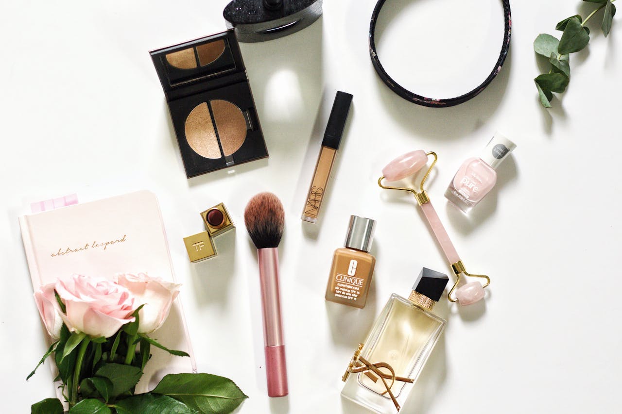 About A stylish flat lay of luxury beauty products including makeup, perfume, and accessories on a white background.