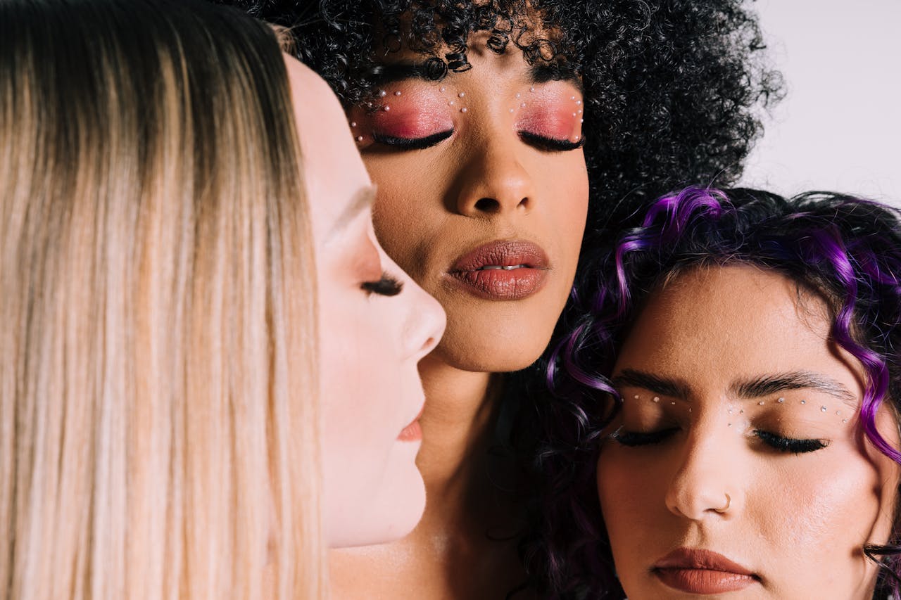Three women with artistic makeup and closed eyes, showcasing fashion beauty.