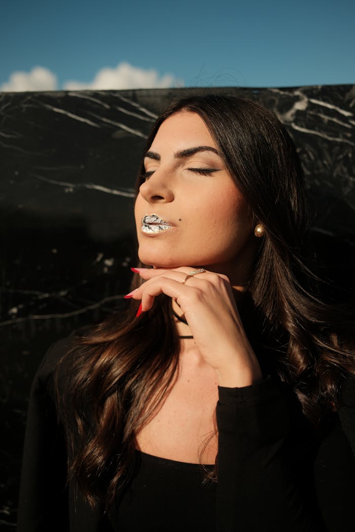 Services Fashionable woman with metallic lipstick posing against a dark marbled background in sunlight.