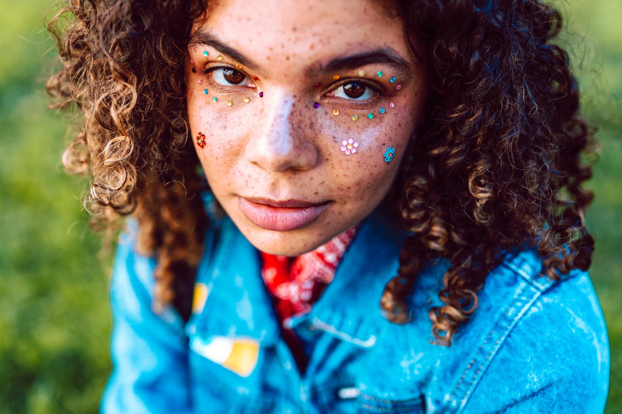 Mastering the First Impression: Your intriguing post title goes here Close-up portrait of a woman with curly hair, freckles, face jewels, and a denim jacket outdoors.