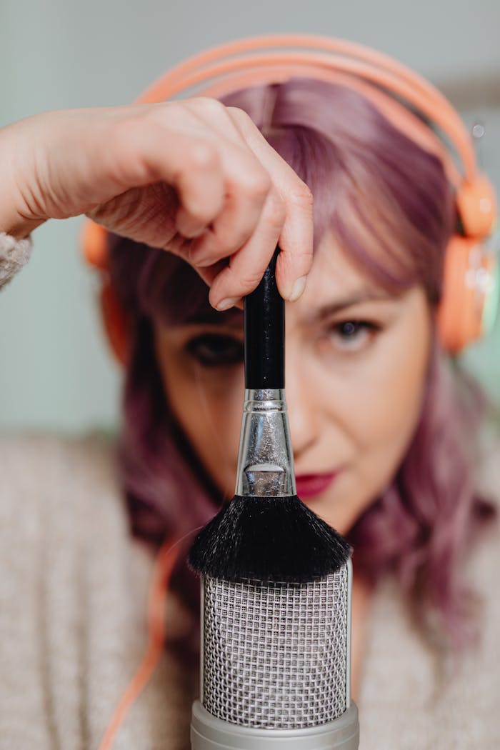 Services Woman with headphones creating ASMR sounds using a brush and microphone.