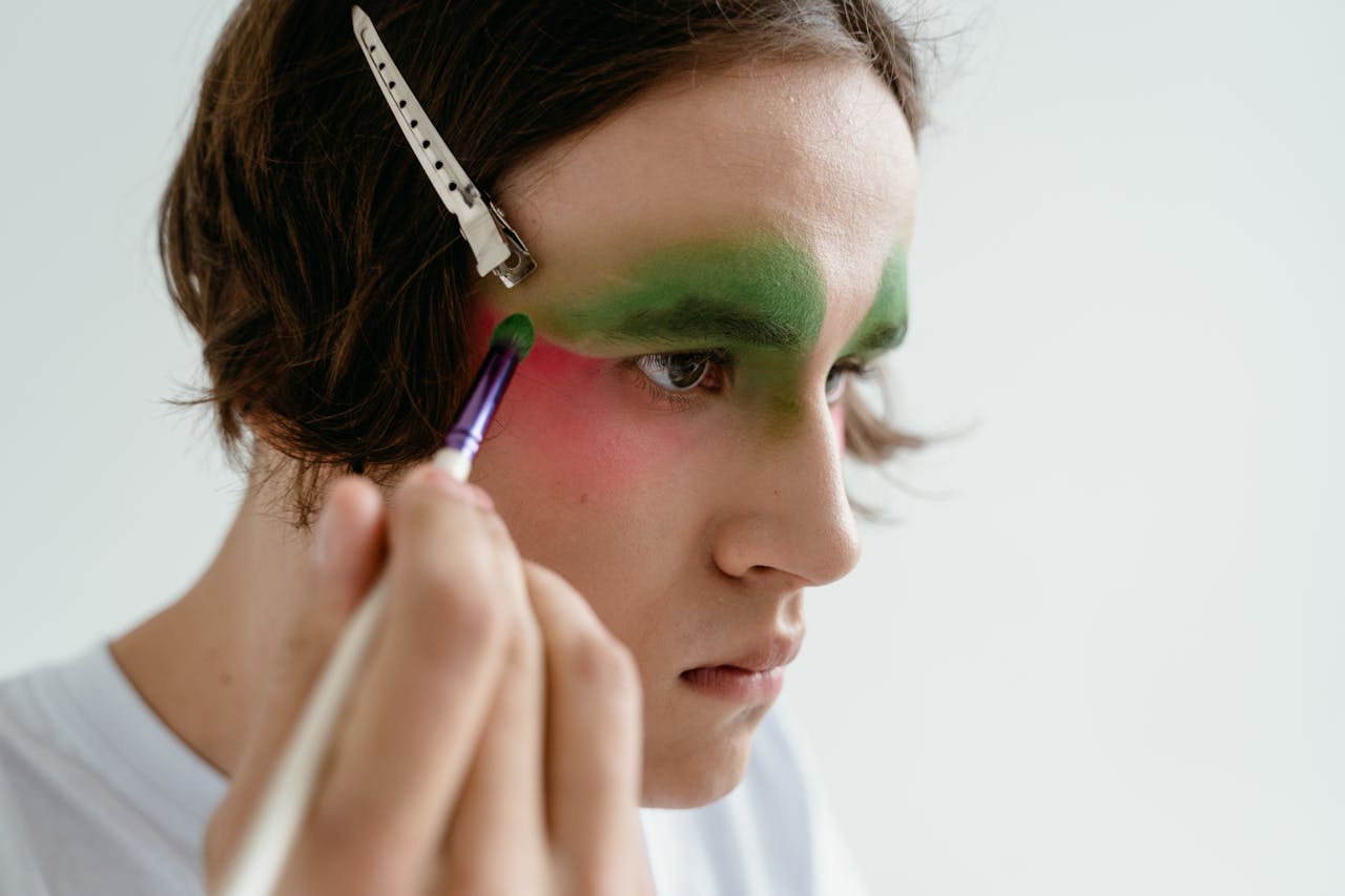Crafting Captivating Headlines: Your awesome post title goes here Close-up portrait of a young person using makeup brush to apply vibrant eyeshadow, with a hair clip on white background.